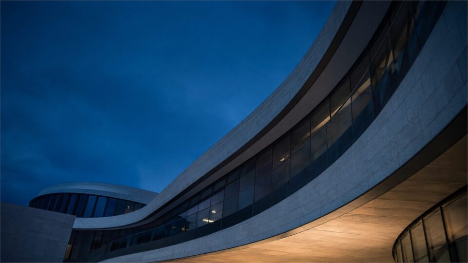 A curved glass office building photographed at blue hour.