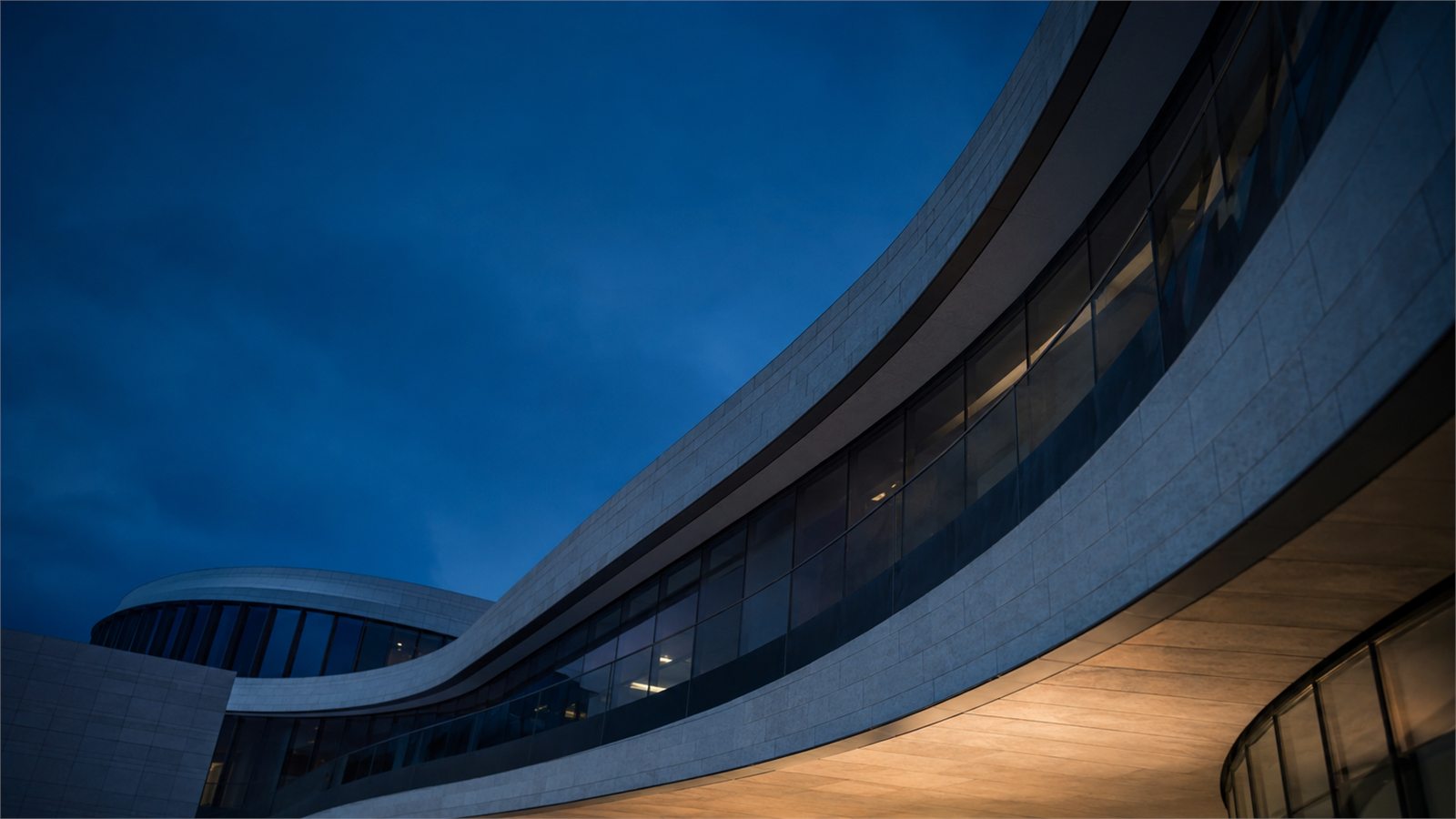 A curved glass office building photographed at blue hour.