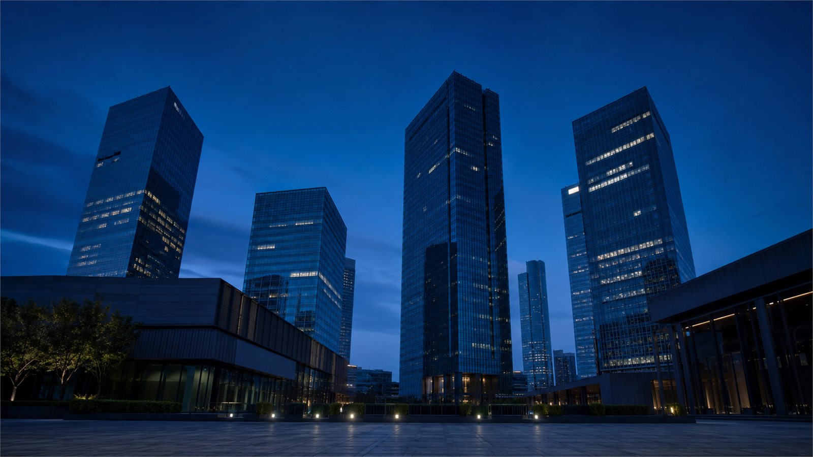 Modern office towers around a public plaza at blue hour.