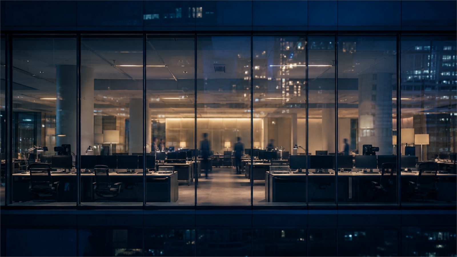A lit newsroom floor seen through the glass facade of an office building at night.
