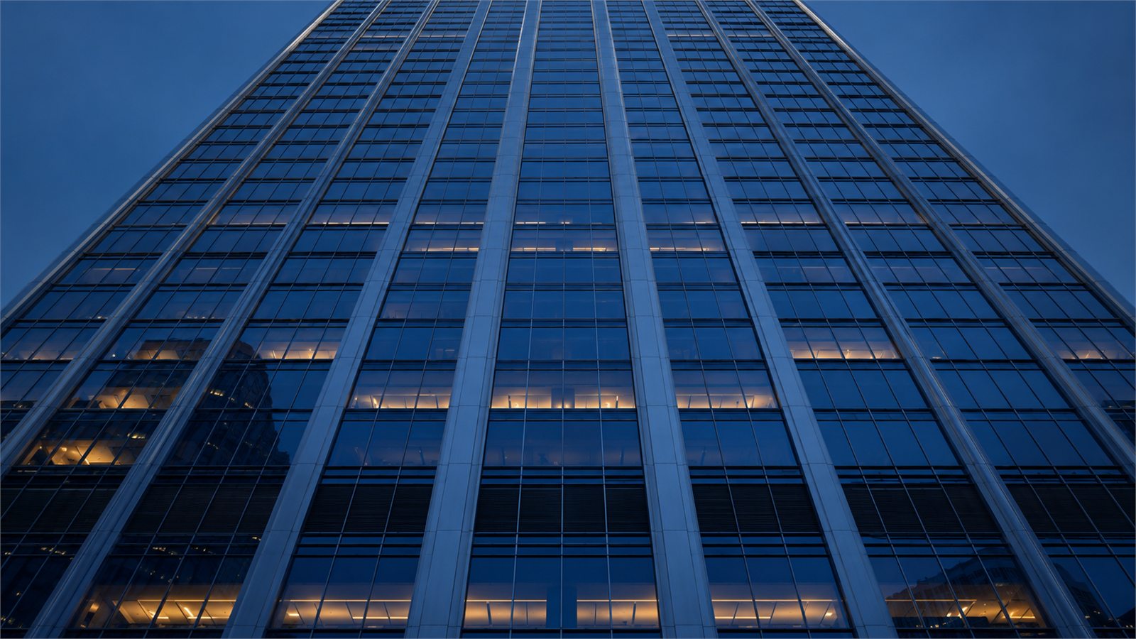 A symmetrical skyscraper facade photographed from below at dusk.
